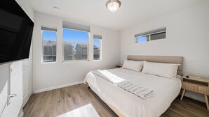 A bedroom with a large bed, a nightstand, a TV, and three windows. - Hummingbird Haven-Prime location in South Longmont-sleeps 8,4beds,blocks to Rec (Longmont)