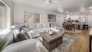 A modern living room with a sectional sofa, a wooden coffee table, and a dining area with a table and chairs. - Hummingbird Haven-Prime location in South Longmont-sleeps 8,4beds,blocks to Rec (Longmont)