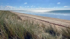 Ein Strand mit Sand und Gras, ein klarer Himmel und ein ruhiges Meer.