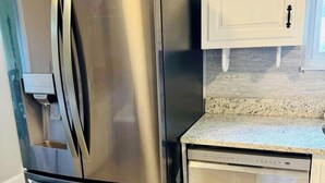 Ein Kühlschrank aus Edelstahl mit Wasserspender, einem Geschirrspüler und weißen Küchenschränken.