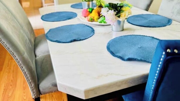 Ein Esstisch mit blauen Platzsets, einer Fruchtschale und einer kleinen Pflanze.
