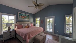 A bedroom with a bed, two bedside tables, a ceiling fan, a window with blinds, and a door. - Angler's Reef : Oceanside Beach, Pool, Sandbar, Kayaks & Boat Slip Available (Islamorada)