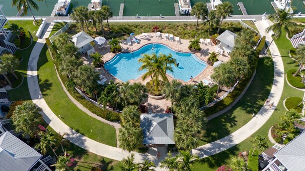 Vista aérea de un complejo turístico con una piscina central, rodeado de palmeras y zonas de descanso.