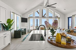 Eine moderne Küche mit einer zentralen Kochinsel, einem Deckenventilator und großen Fenstern mit Blick ins Freie.