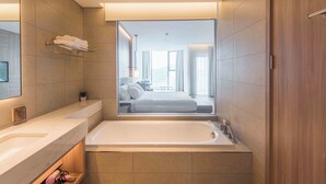 Ein modernes Badezimmer mit einer großen Badewanne, einem Spiegel und Blick in das Schlafzimmer.