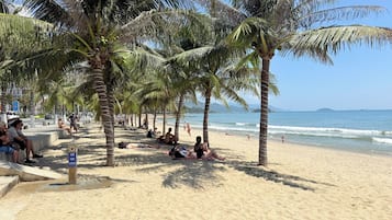 A beach with palm trees, people relaxing, and a clear sky.