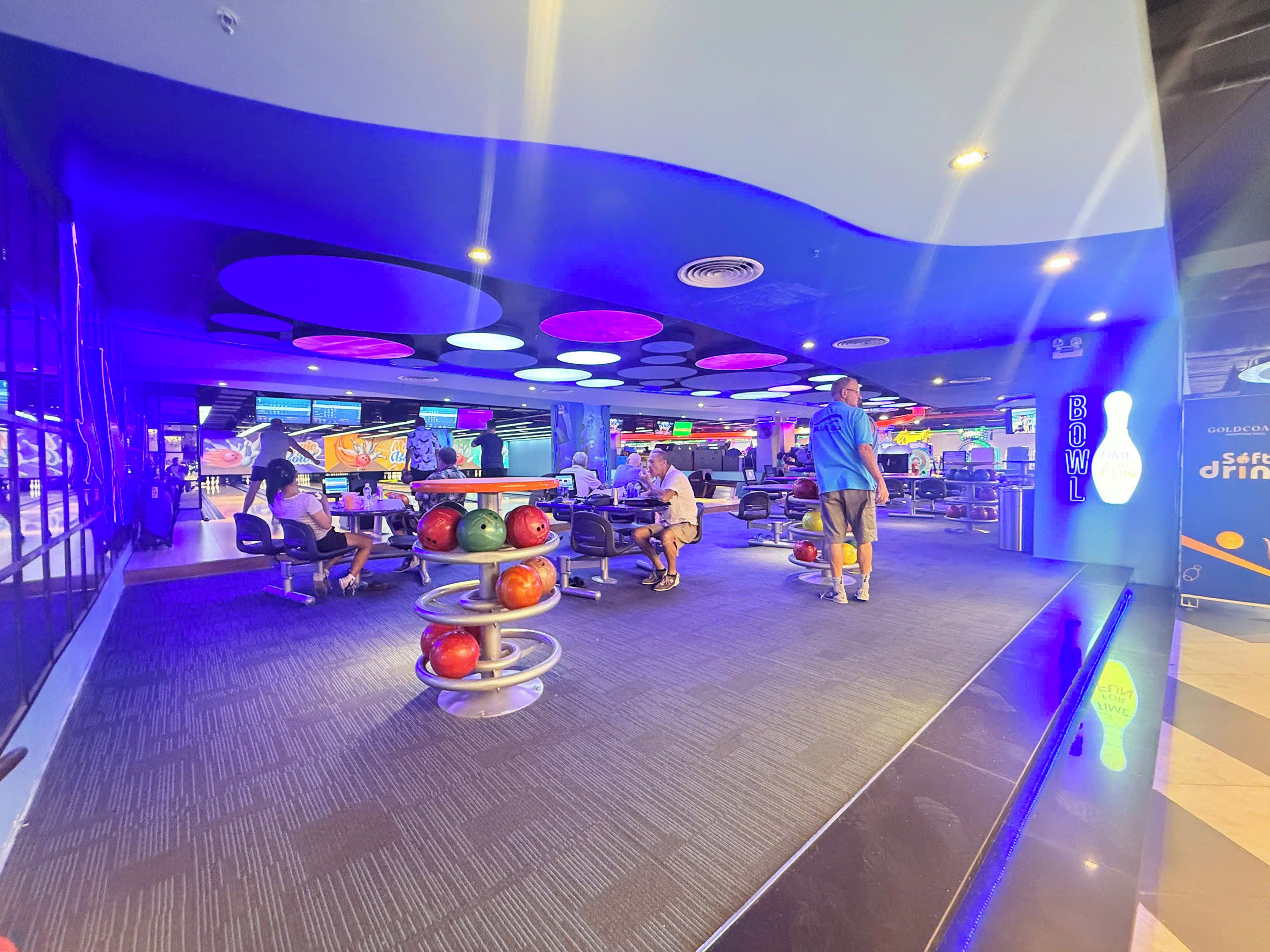 Une salle de bowling avec plusieurs pistes, un présentoir à boules de bowling et un panneau lumineux au néon.