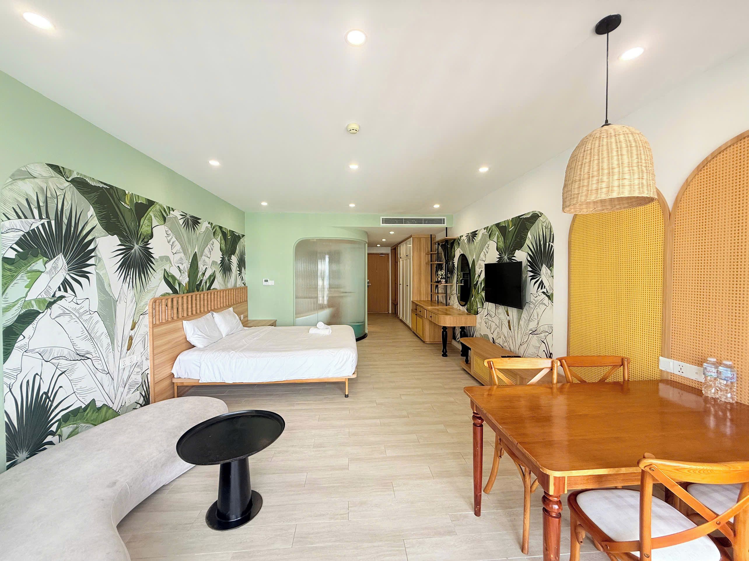 A hotel room with a bed, a dining table, a sofa, a TV, and a shower area.