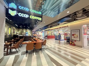 Una cafetería moderna con una barra larga y varias mesas, un cartel de menú visible y un techo con un diseño geométrico.