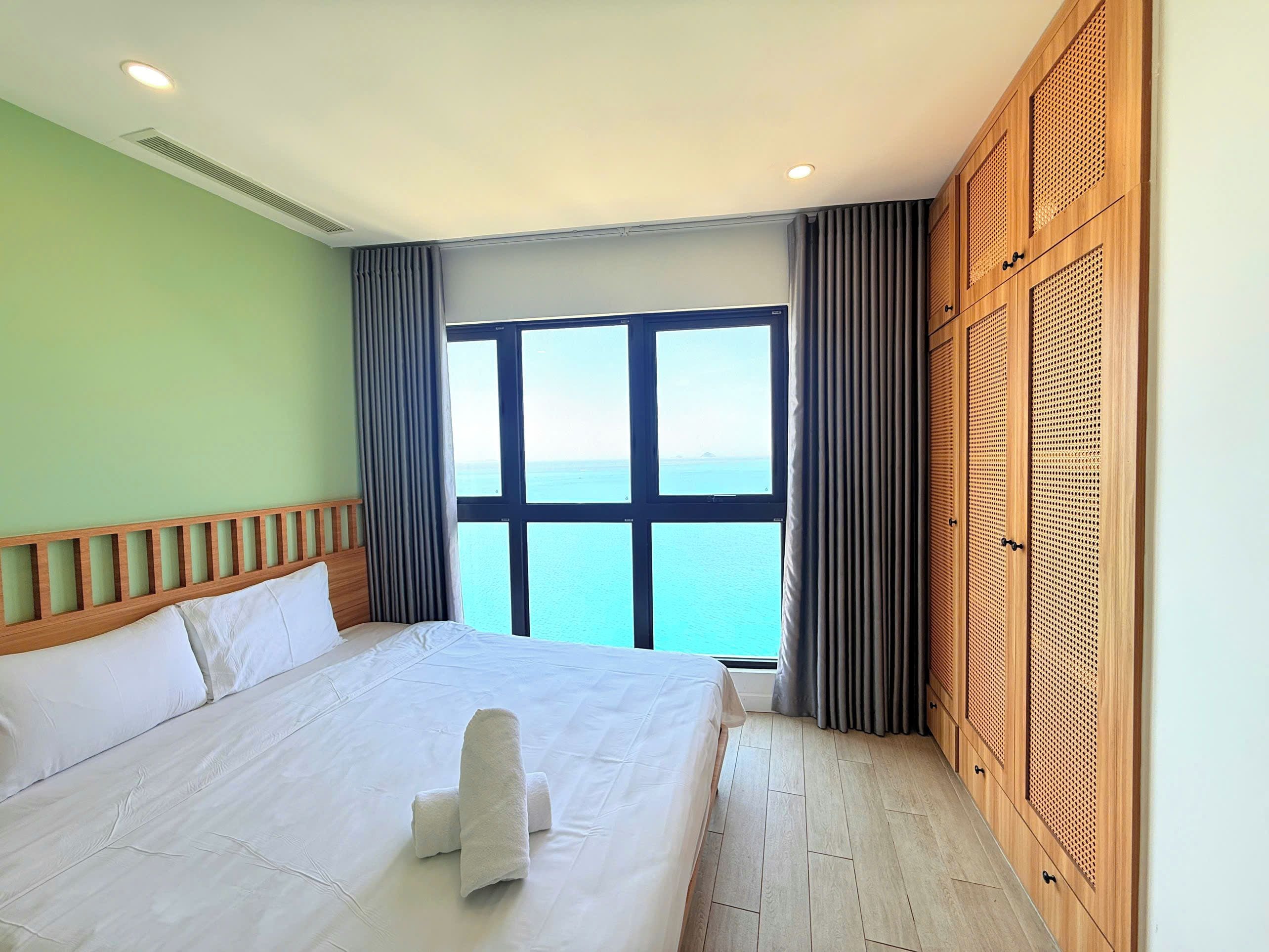 A hotel room with a large bed, a view of the sea, and a wooden wardrobe.