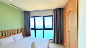 A hotel room with a large bed, a view of the sea, and a wooden wardrobe.