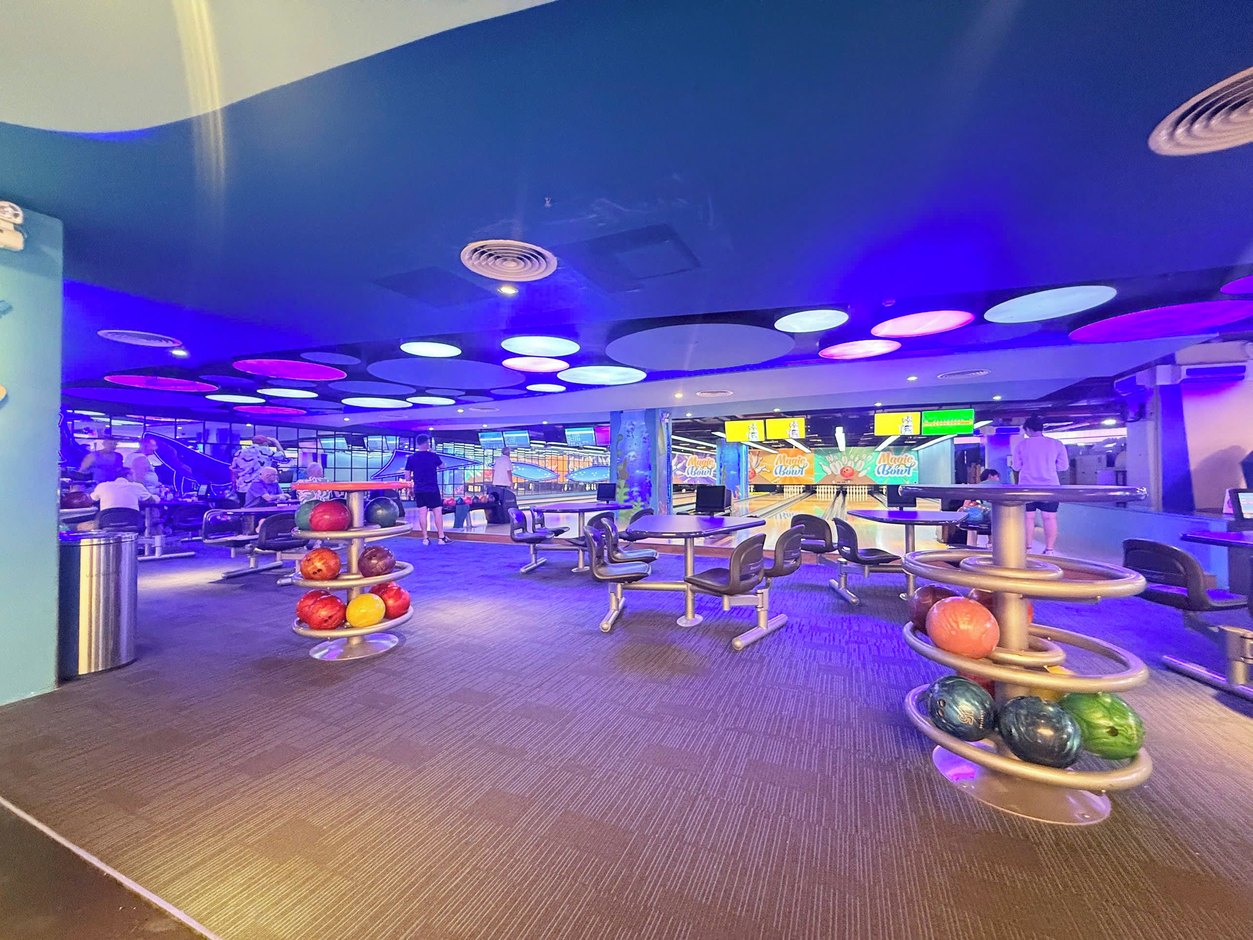 A bowling alley with multiple lanes, seating areas, and a brightly lit ceiling.