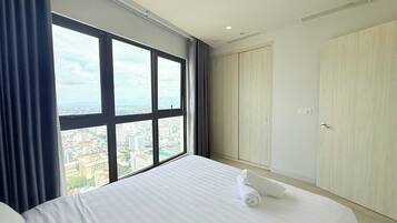 Habitación de hotel con un ventanal grande, cama, armario y vista a la ciudad.
