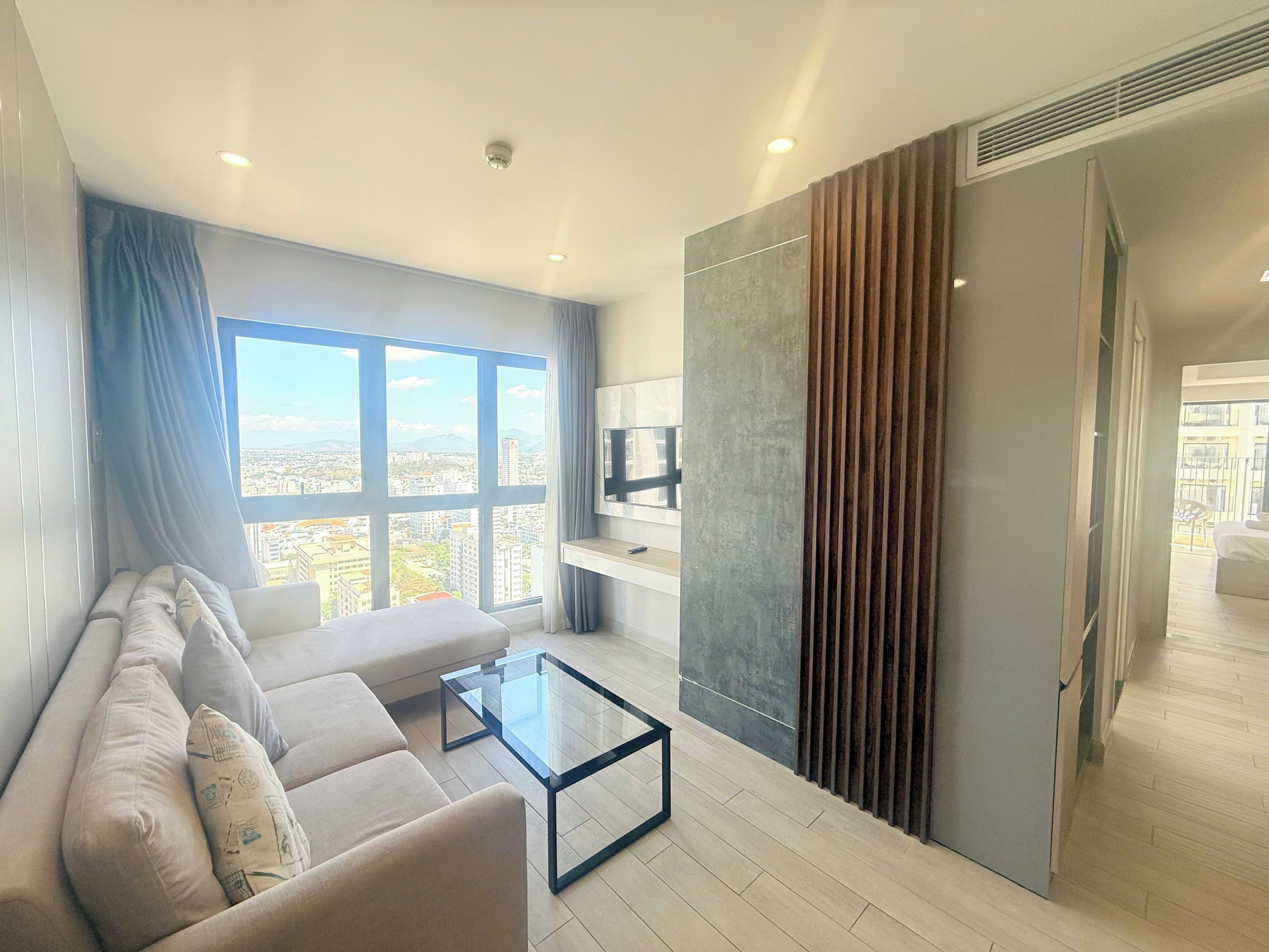Ein modernes Wohnzimmer mit einer Couch, einem Glastisch und einem großen Fenster mit Blick auf die Stadt.