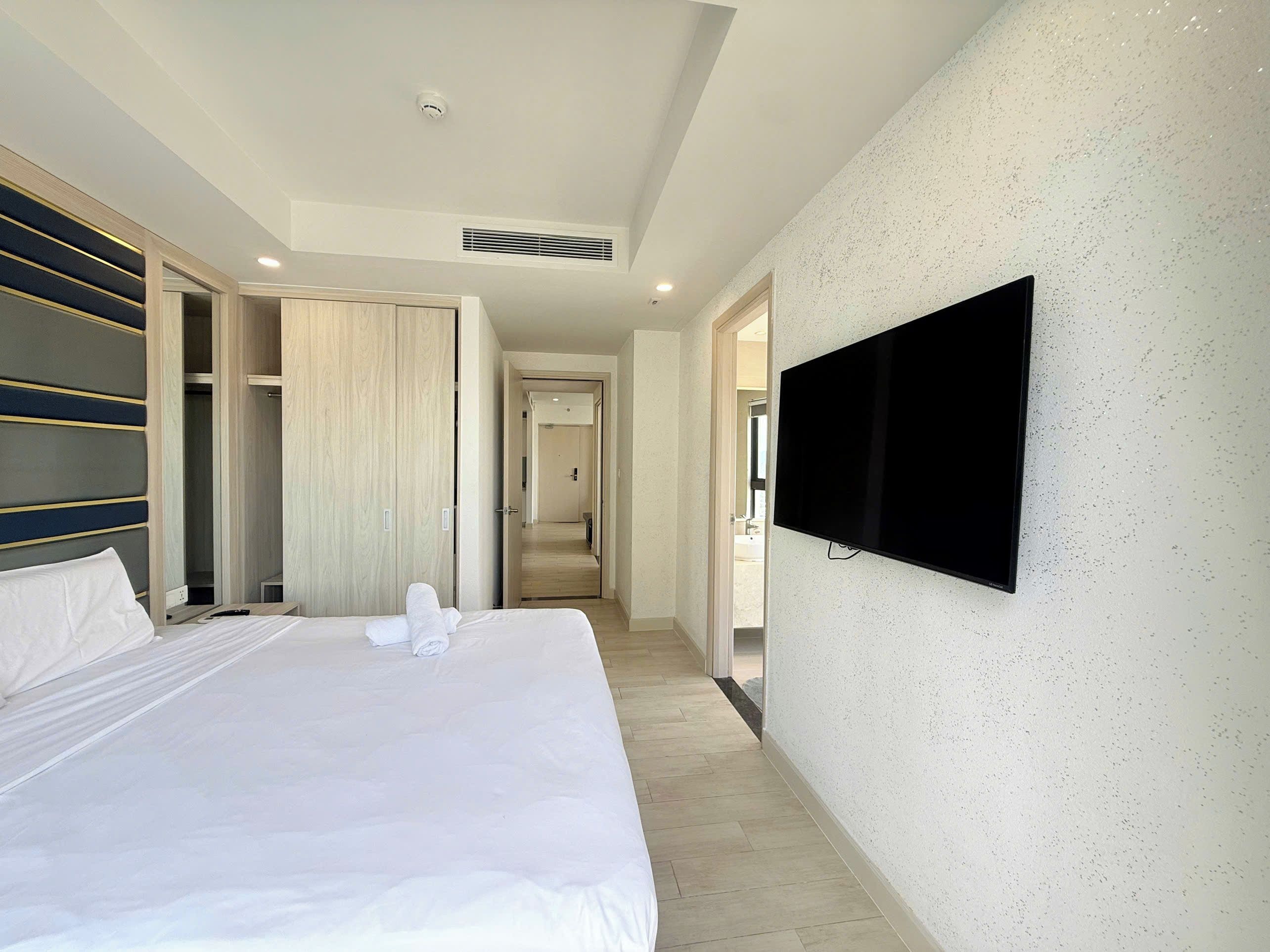 Une chambre d’hôtel avec un lit, un téléviseur fixé au mur et un dressing.