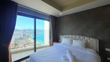 A hotel room with a large bed, a view of the sea, and a balcony with a railing.
