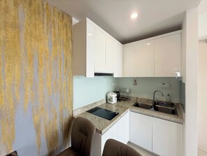 A compact kitchen with white cabinets, a granite countertop, a sink, and a kettle. - Apartment With Seaview (Nha Trang)