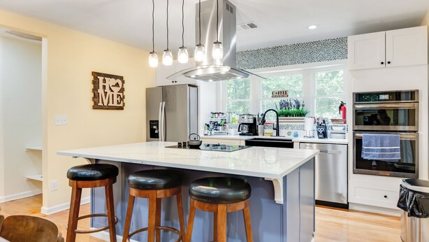 A modern kitchen with a central island, bar stools, stainless steel appliances, and a decorative backsplash. - Dew Drop Inn | 4BR Retreat | Lakeside | Hot Tub (Quinton)