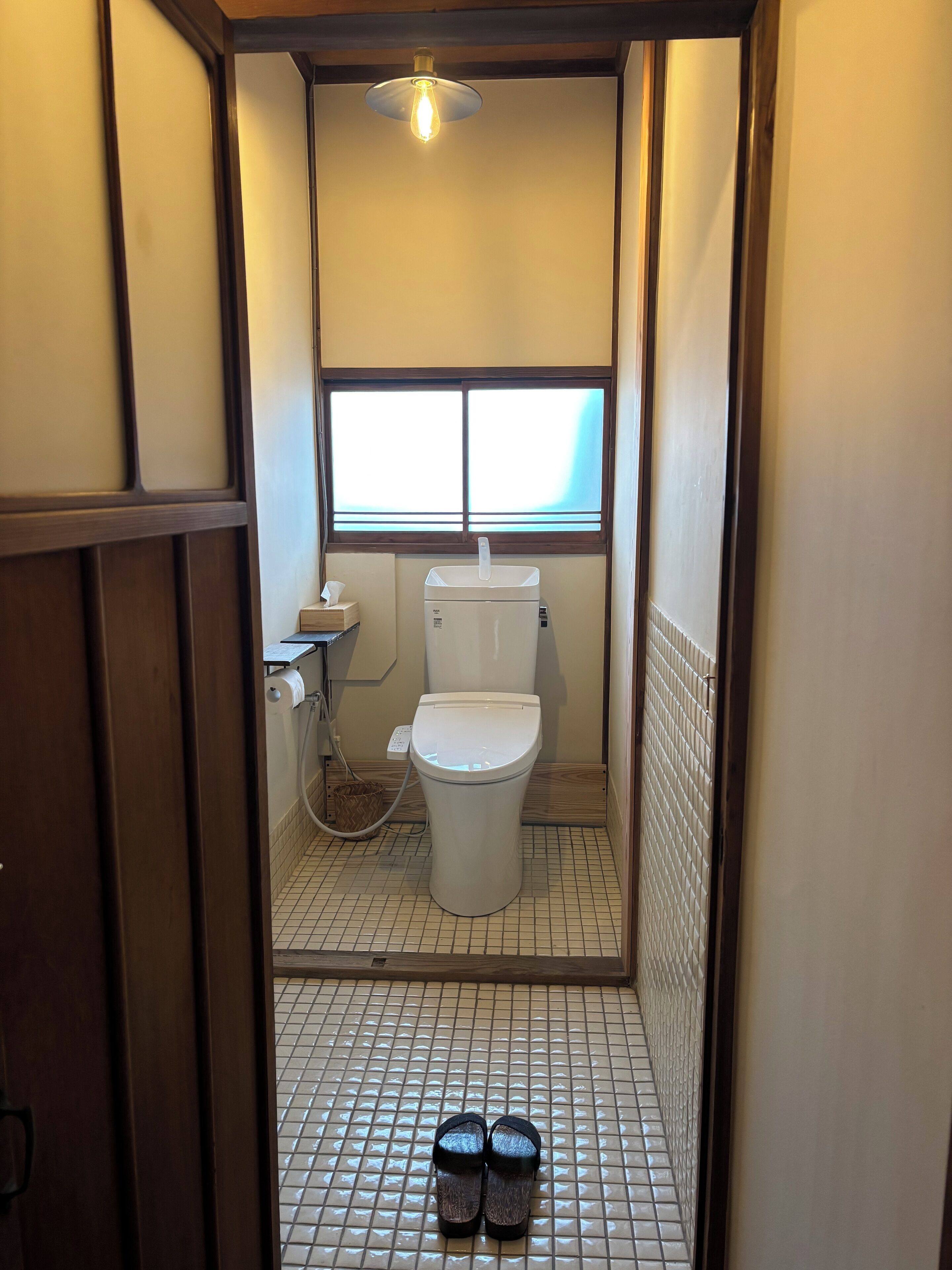Een kleine, smalle badkamer met toilet, raam en betegelde vloer.