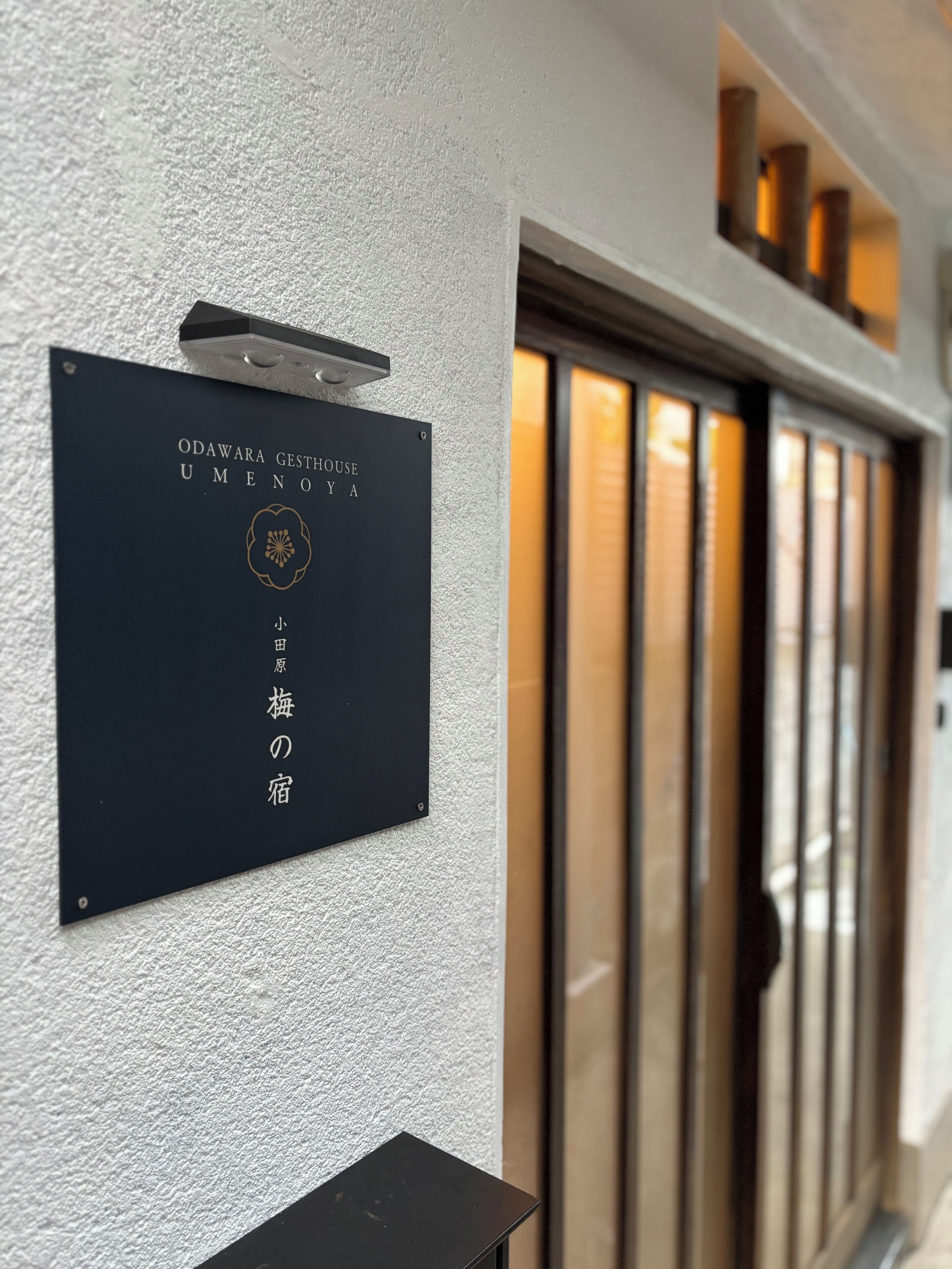 Un cartel con texto japonés que indica una casa de huéspedes llamada 'Odawara Gesthouse Umenoya' de 'Kobayashi'.