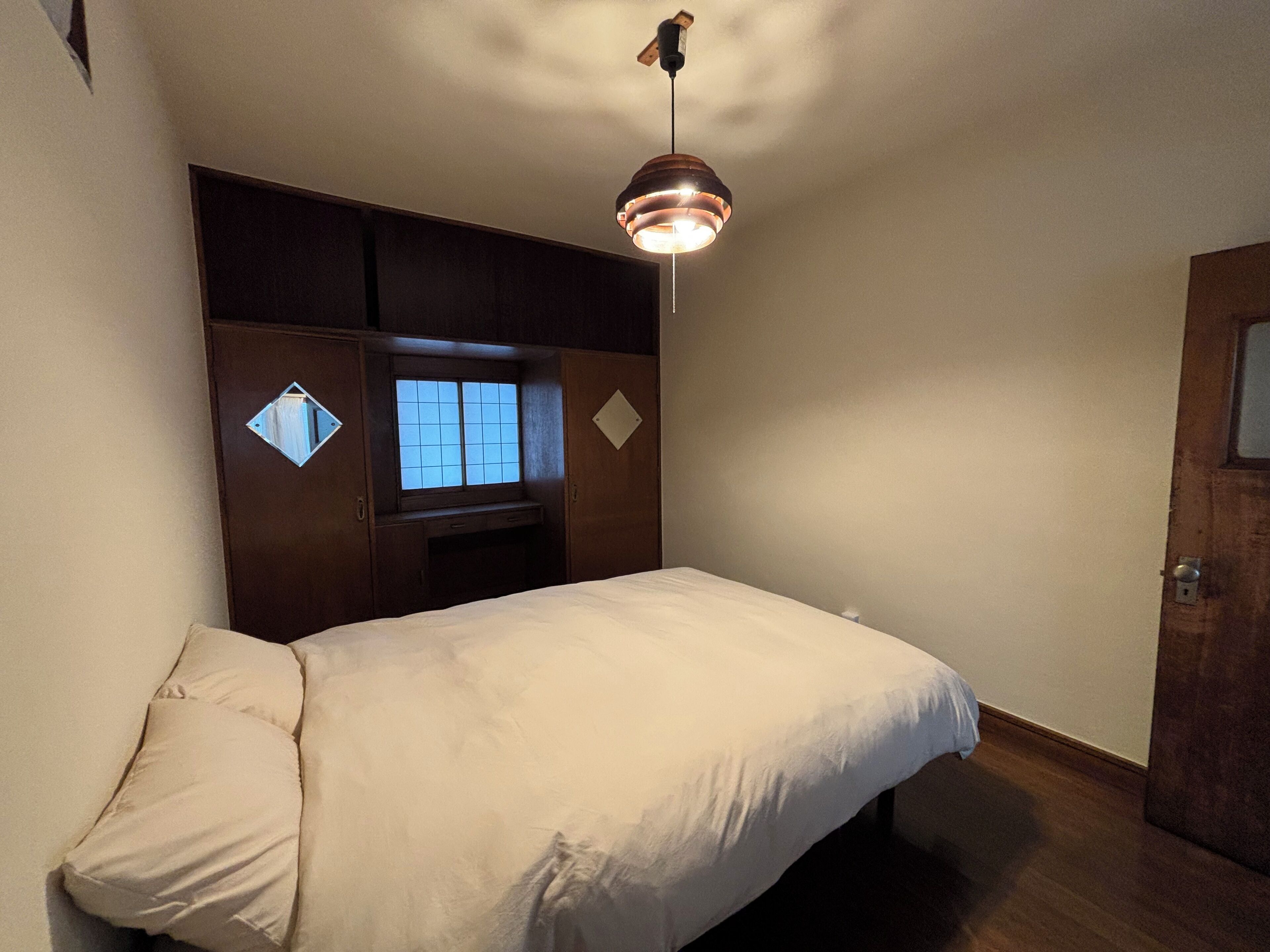 A bedroom with a bed, a window, a wardrobe, and a hanging light fixture.