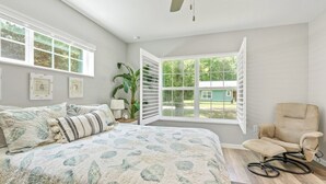 Ein Schlafzimmer mit einem großen Bett, einem Sessel, einem Fenster mit Jalousien und einem Deckenventilator.