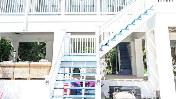 Ein weißes, zweistöckiges Gebäude mit einem Balkon im oberen Geschoss und einer Treppe, die zum unteren Bereich führt.