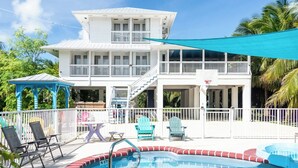 Ein zweistöckiges Haus mit Pool, Sitzgelegenheiten im Freien und einer überdachten Fläche.