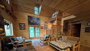A log cabin interior with a loft bedroom, wooden furniture, and a large window. - Cozy Private Lakefront Terry Redlin-Style Cabin w/ Unique Loft (Brainerd)