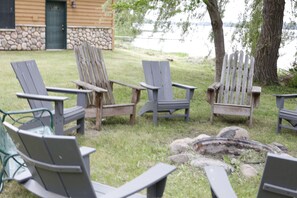 Nurmikkoalueella on nuotiopaikka, jonka ympärillä on Adirondack-tyylisiä puutarhatuoleja. Taustalla näkyy kivimuuri ja puinen rakennus.