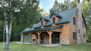A lodge with a stone chimney, a covered porch, and a picnic table. - Cozy Private Lakefront Terry Redlin-Style Cabin w/ Unique Loft (Brainerd)