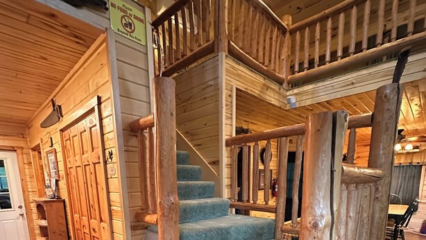 A wooden staircase with a handrail, carpeted steps, and a sign indicating no food or drink beyond a certain point. - Cozy Private Lakefront Terry Redlin-Style Cabin w/ Unique Loft (Brainerd)