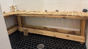 Un baño en esquina con un banco de madera, un pequeño osito de peluche blanco y un suelo hexagonal negro.
