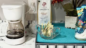 A kitchen counter with a coffee maker, a glass bowl with napkins, a tissue box, a potted plant, and a packet of liquid soap.