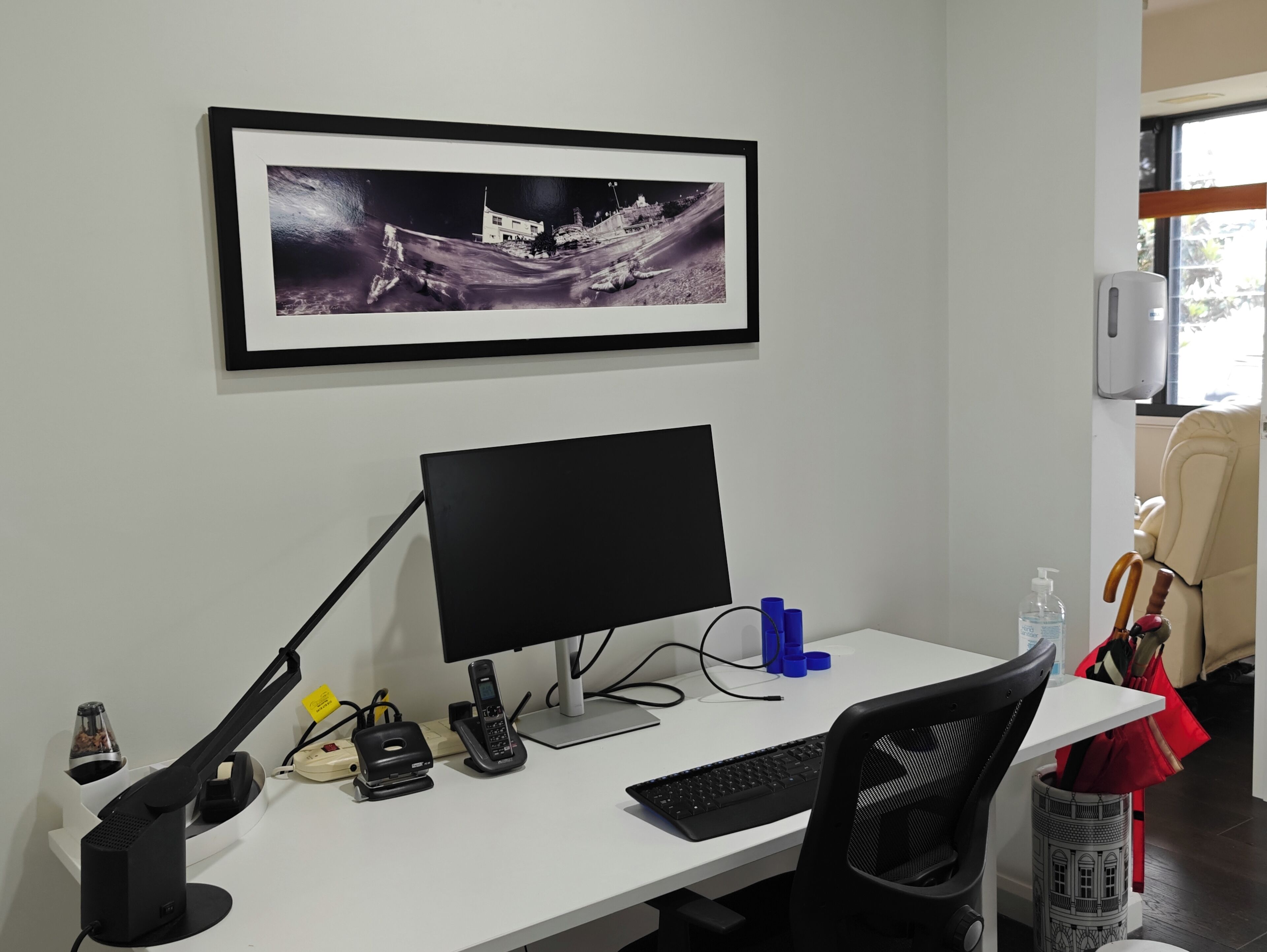 A workspace with a desk, computer, phone, and a framed picture on the wall.