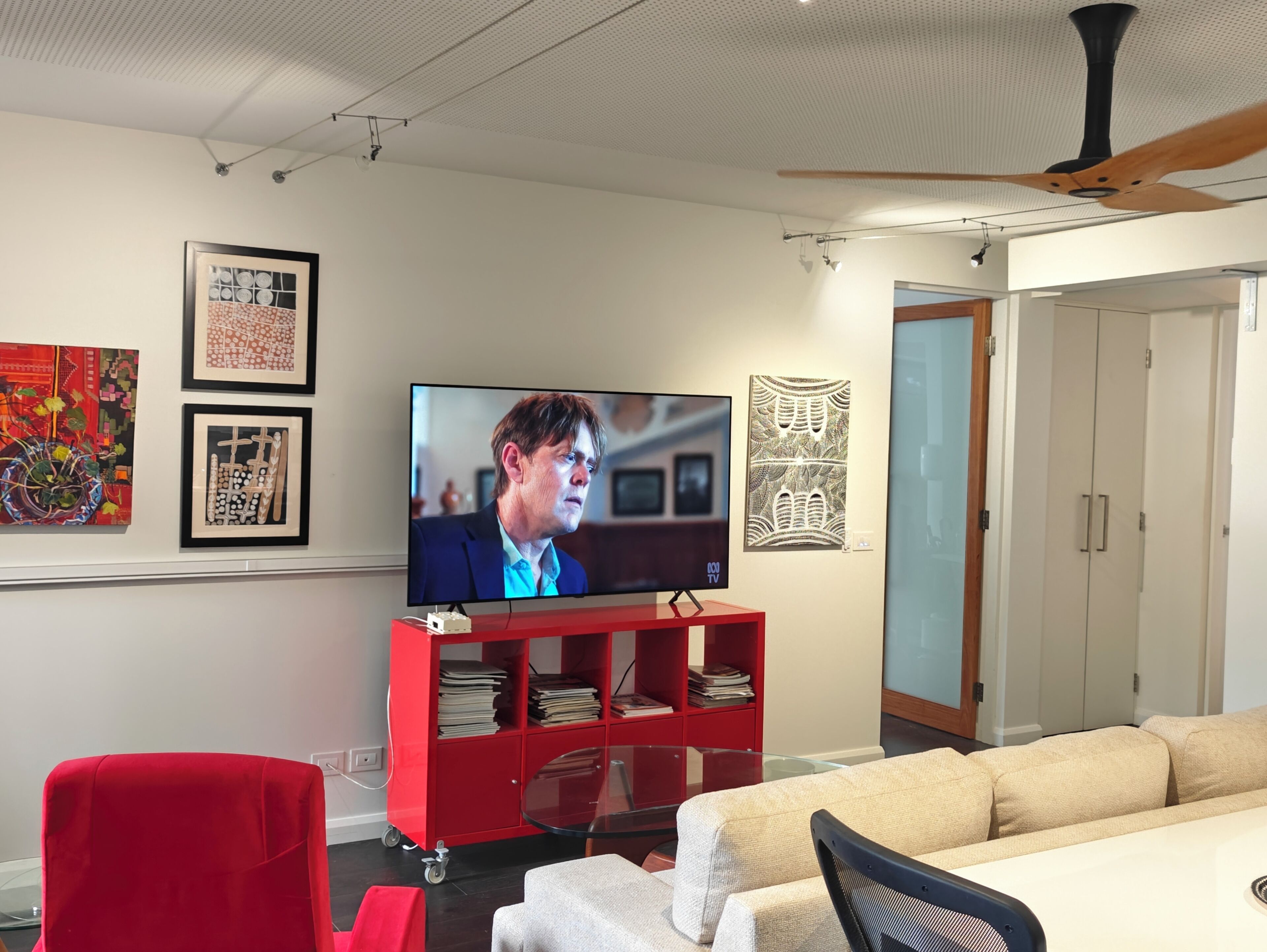 A modern living room with a flat-screen TV, red shelving unit, and a beige sofa.