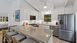 A modern kitchen with white cabinets, a stainless steel refrigerator, a large island with bar stools, and a ceiling fan. - Private Pool | 2 Mins to Beach | Walk to Dining (St. Thomas)