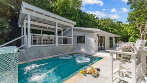 A pool area with a covered seating area, a white building with a window, and a clear blue pool. - Private Pool | 2 Mins to Beach | Walk to Dining (St. Thomas)