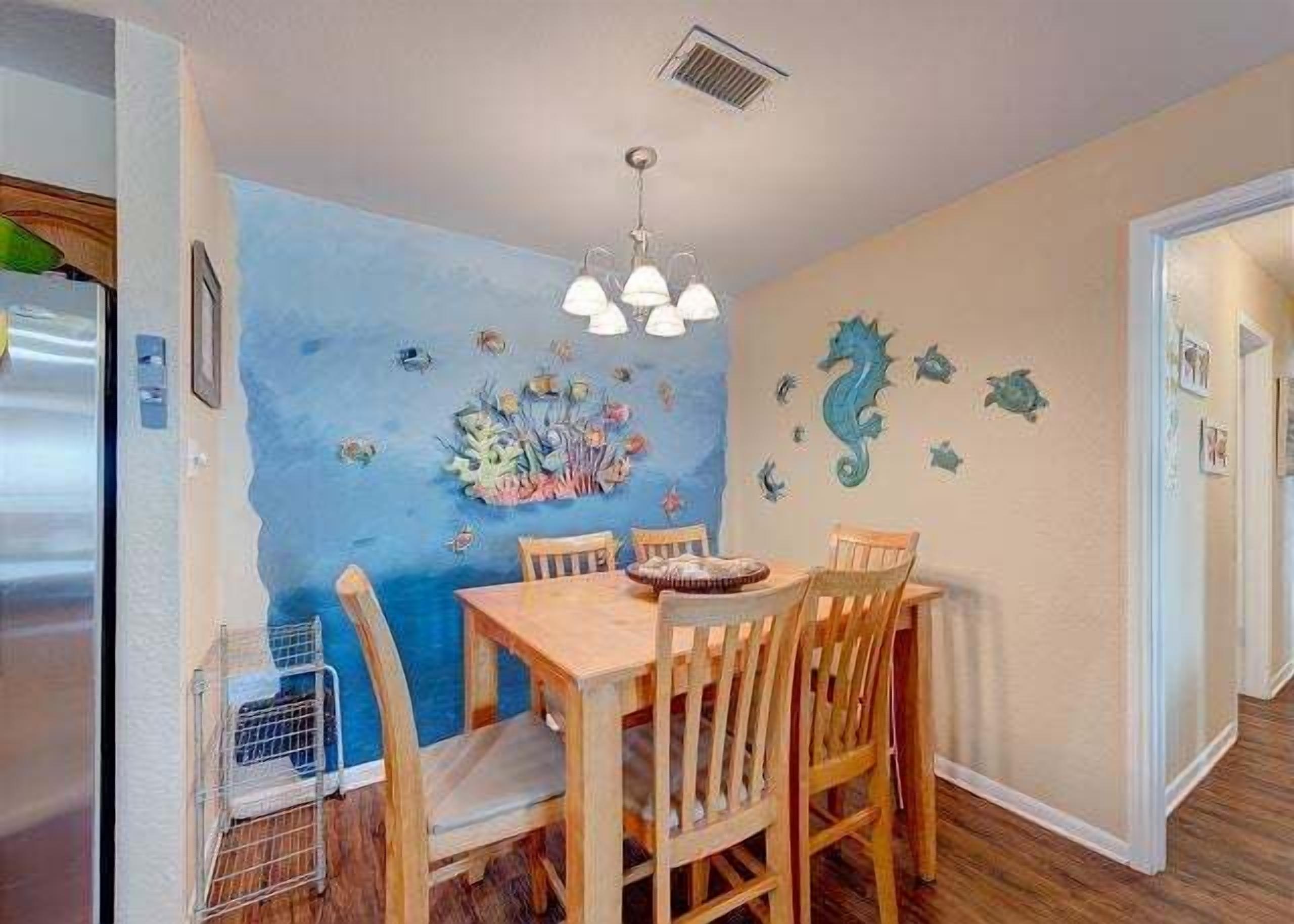 A dining area with a blue wall mural, wooden table and chairs, and a ceiling light fixture.