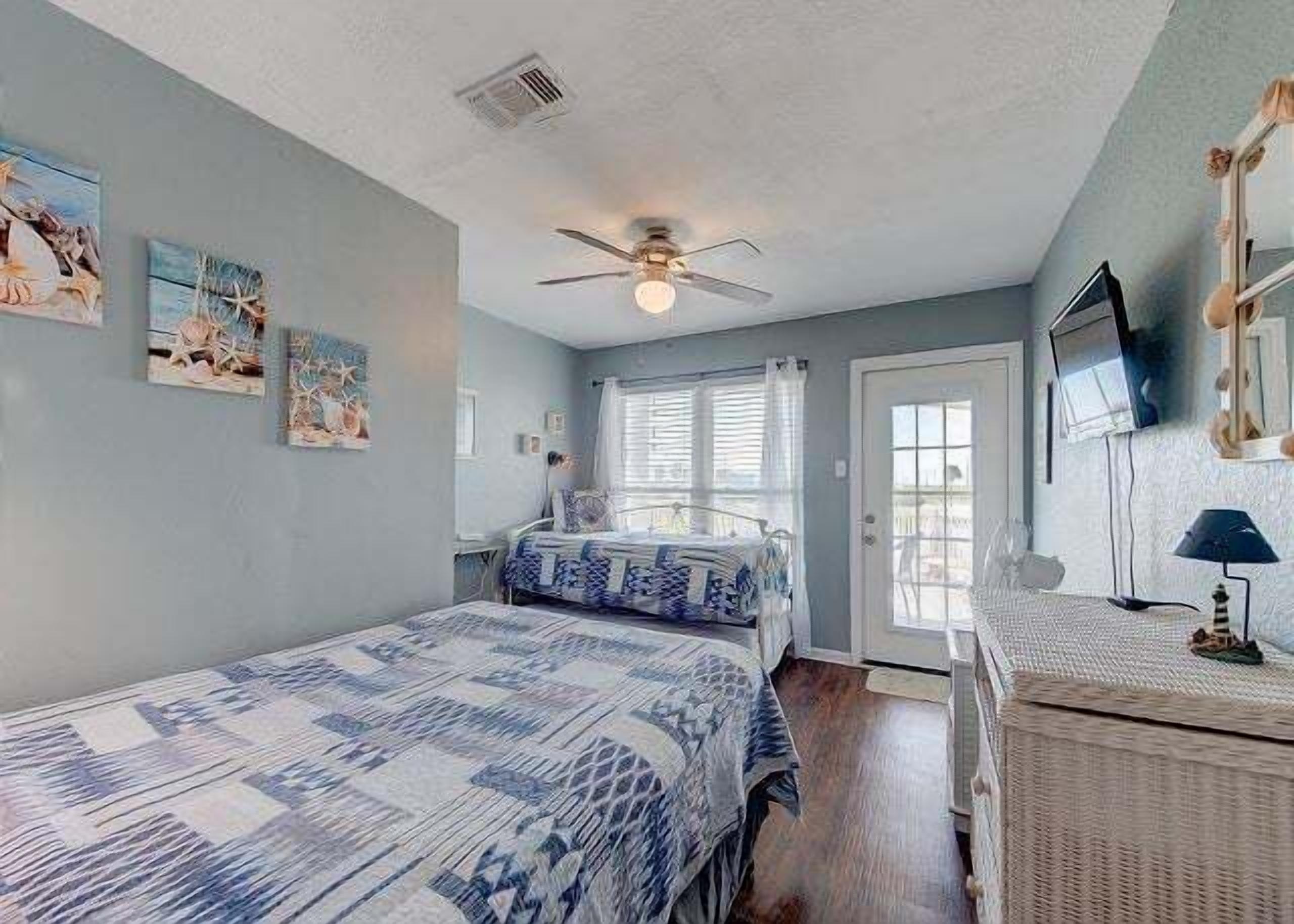 Une chambre à coucher avec un lit, un ventilateur de plafond, une fenêtre et un téléviseur fixé au mur.