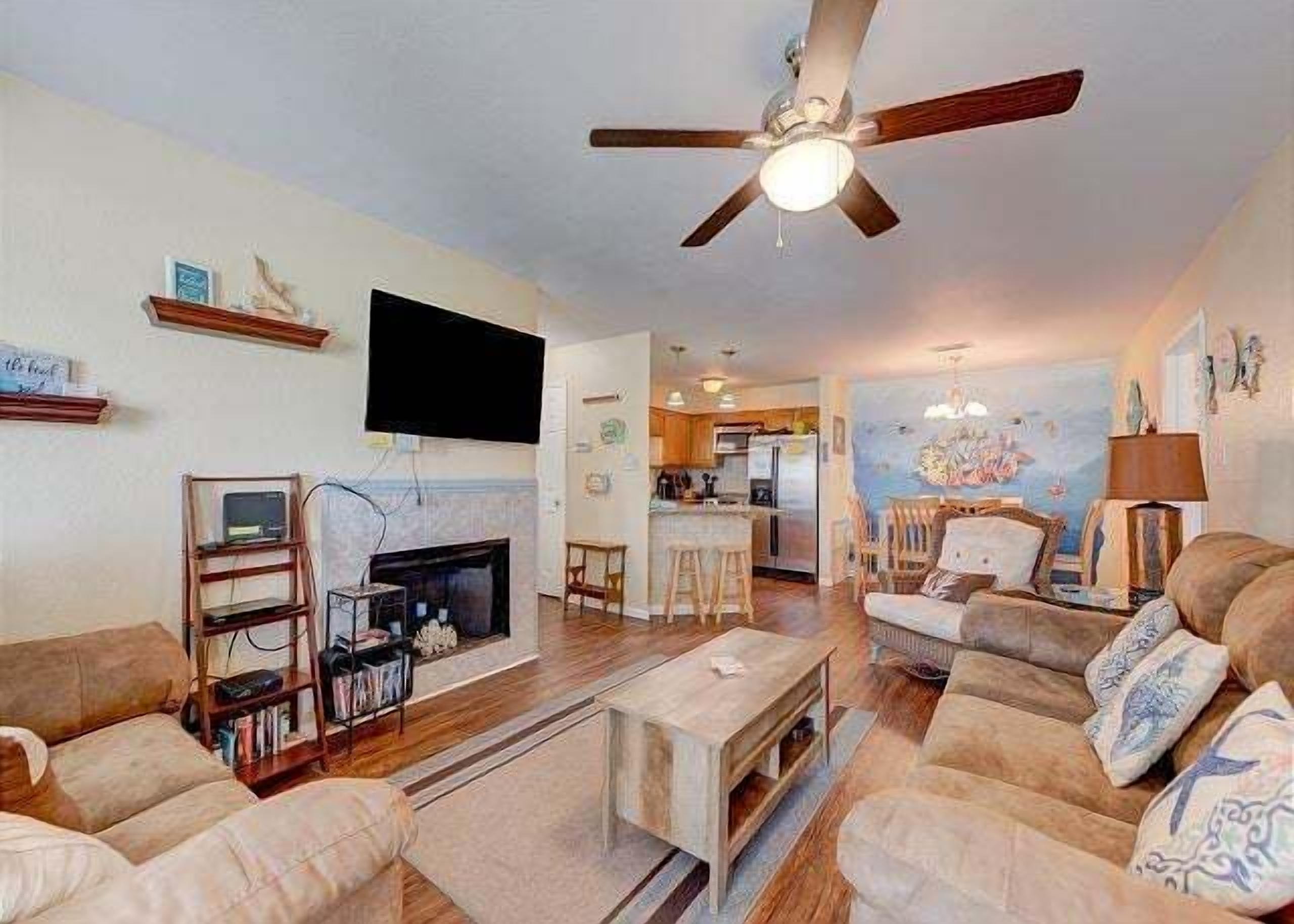 A living room with a fireplace, a television, and a ceiling fan.
