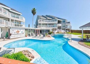 A swimming pool with a sun deck, a covered area, and a multi-story building with balconies. - Shared Pool, Hot Tub, Boardwalk to the Beach (Port Aransas)