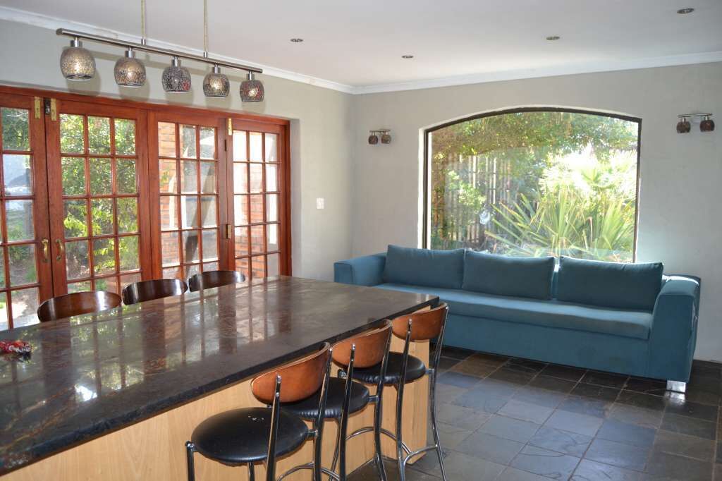 A kitchen with a large island, bar stools, a blue sofa, and a large window with a view of greenery.