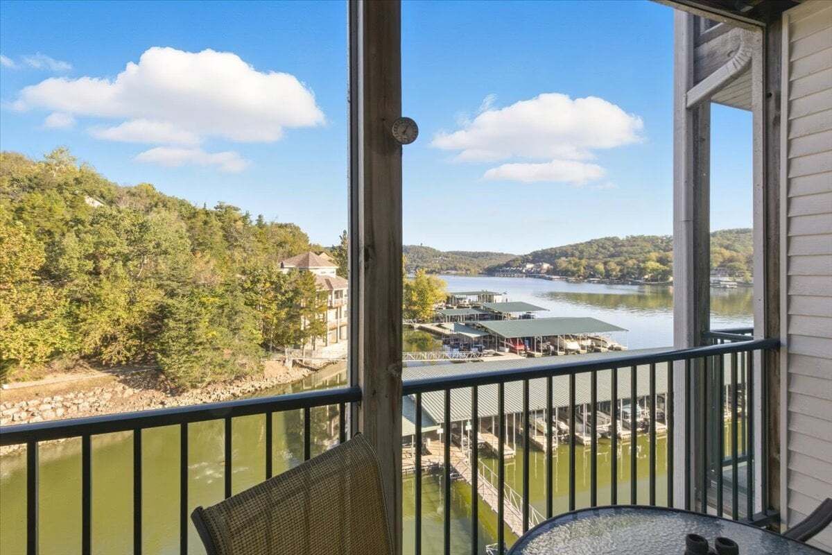 Un balcon offrant une vue sur une rivière, un quai et des bâtiments situés de l’autre côté.
