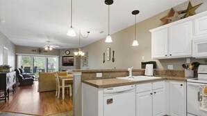 A kitchen with white cabinets, a countertop, and a sink. There is a dining area with a table and chairs.