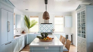 Una cocina moderna con armarios azul claro, una isla central con un frutero y una lámpara colgante.