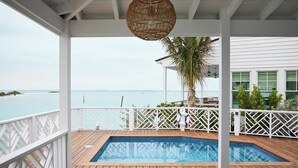 Una terraza de madera con piscina, barandillas blancas y vista al mar.