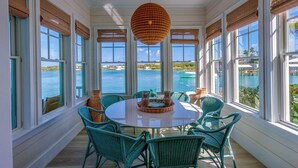 A round table with chairs in a room with large windows overlooking a body of water. - 3 bedroom Villa - Sunset Point, Abaco - Surf Inn Villa # 2 (Elbow cay)