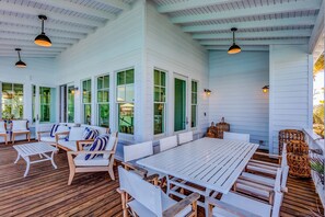Une terrasse extérieure dotée de meubles en bois, de grandes fenêtres et de luminaires suspendus.