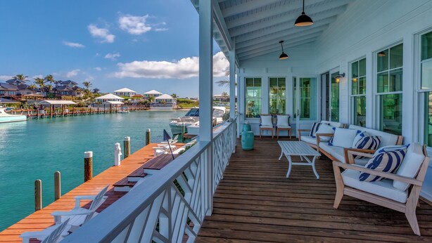A covered deck with wooden flooring, white railings, and seating areas with cushions. - 3 bedroom Villa - Sunset Point, Abaco - Surf Inn Villa # 2 (Elbow cay)